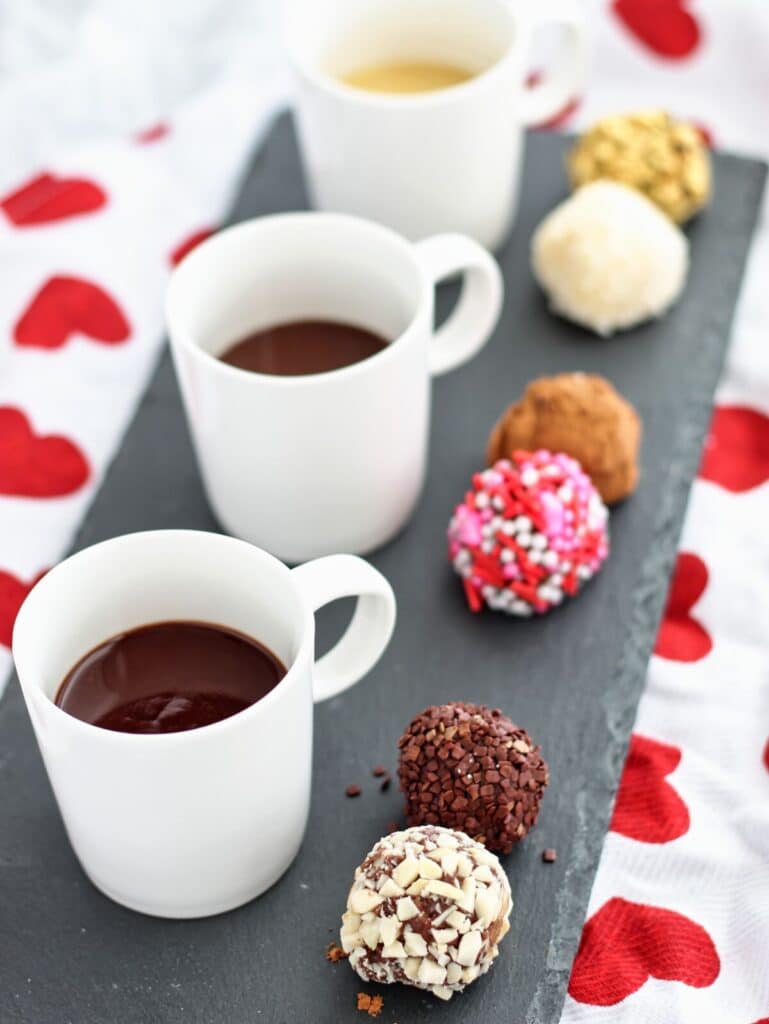 row of sipping chocolate flight and truffle flight on black slate rectangular platter over a red heart towel.