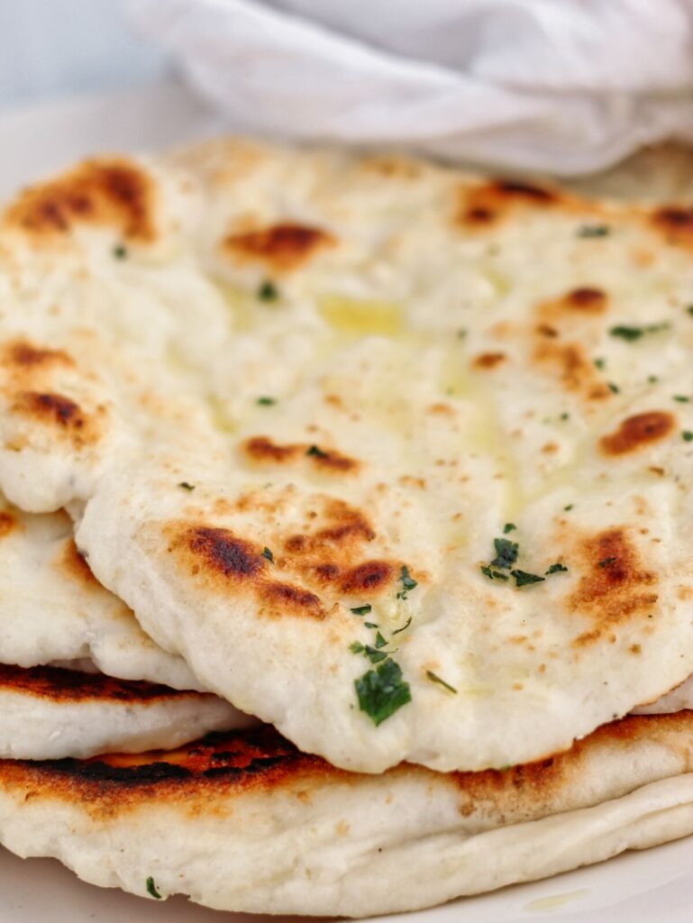 pile of whole gluten free yeasted naan on white platter wrapped in white towel.