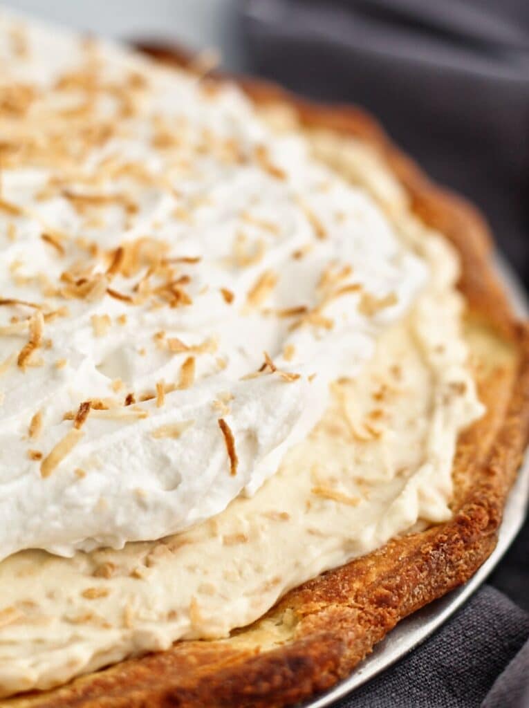 side view of close up of partial triple layer coconut pie with grey towel on the side.