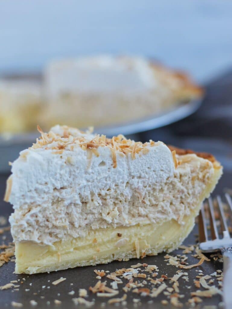piece of triple layer gluten free coconut cream pie on black square plate sprinkled with toasted coconut.