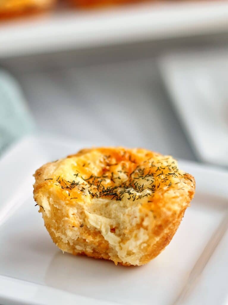 up close bite shot of one gf cheddar dill tartlet on small white square plate.