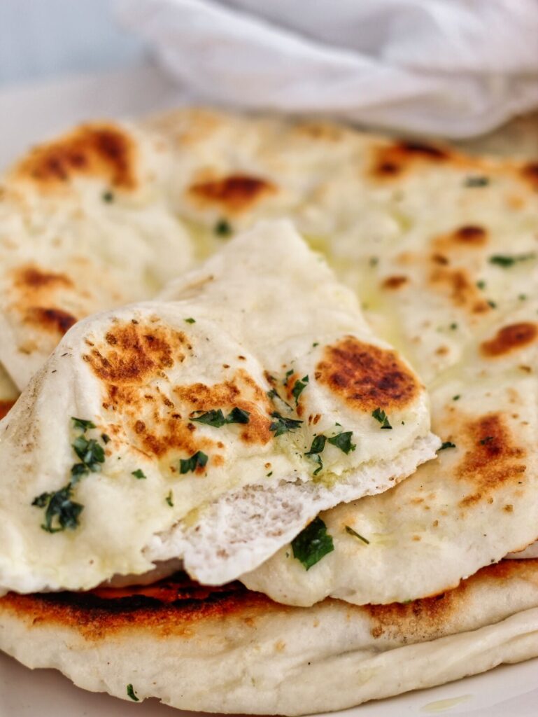 piece of torn apart gluten free yeasted naan on a stack of whole naan wrapped in a white tea towel.