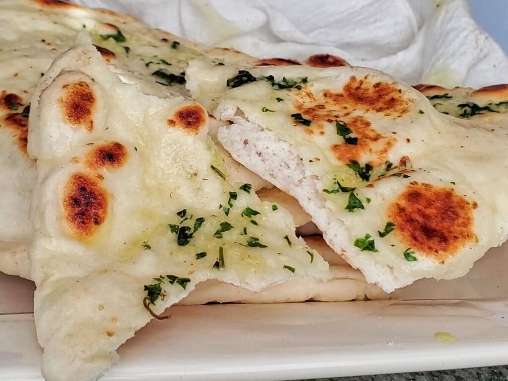 gluten free naan bread torn in half on top of pile of whole naan on white platter.
