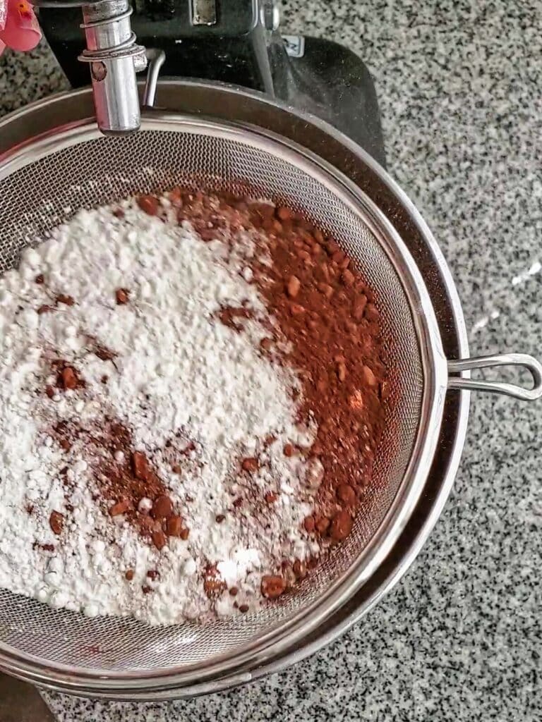 sifting cocoa powder and gluten free flour in sieve over kitchenaid mixing bowl.
