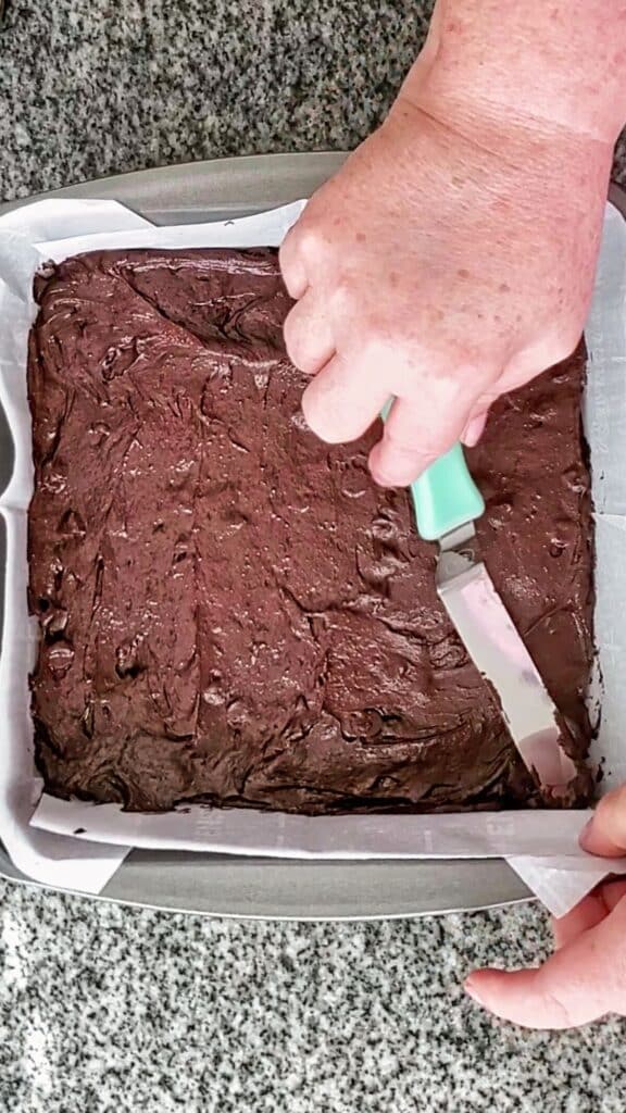 spreading brownie batter in square baking pan.