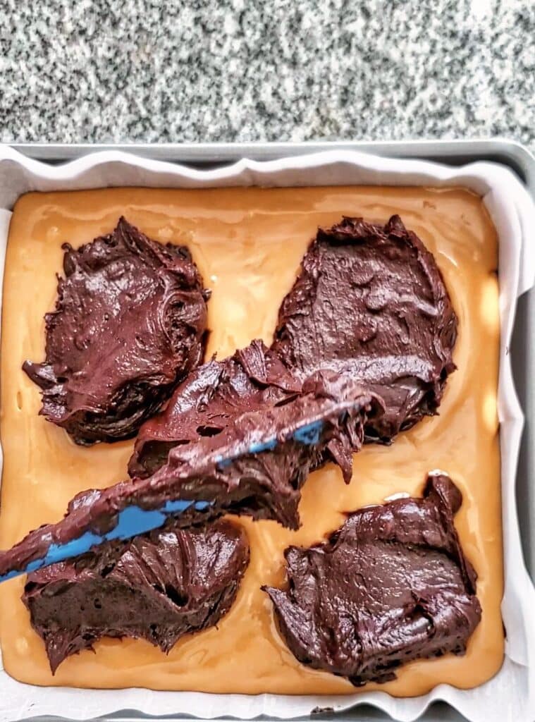 dolloping rest of brownie batter on top of caramel layer in square pan.