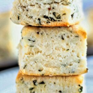 three stacked gluten free basil biscuits on a white plate.