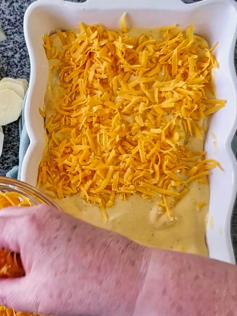 layering shredded cheddar cheese on top of sauce layer in casserole dish.