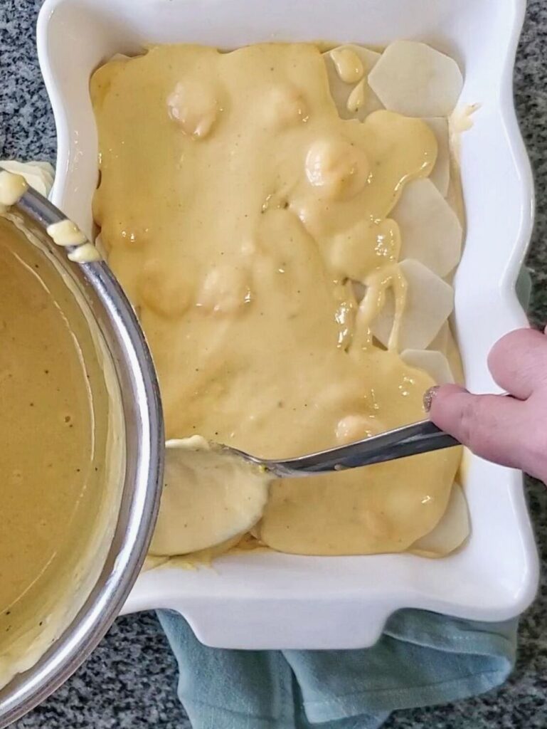 adding cheese sauce on top of potato layer in casserole dish.