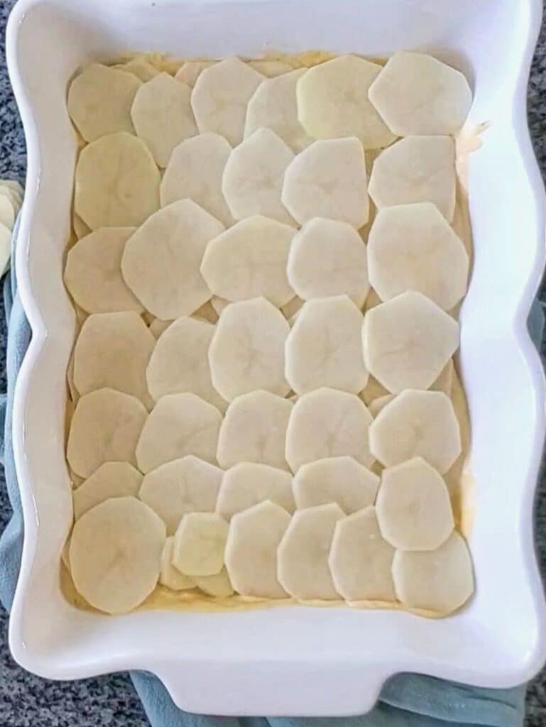 layering potatoes into white rectangular casserole dish.