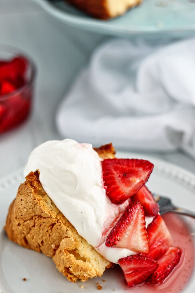 slice of pound cake on white plate with whipped cream and strawberries on top.