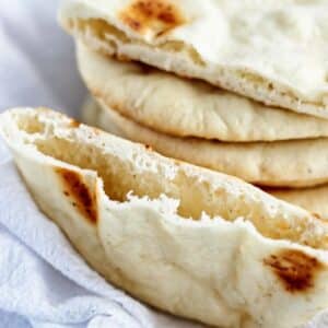 stack of gf pita bread on white towel with one cut in half to show pocket.