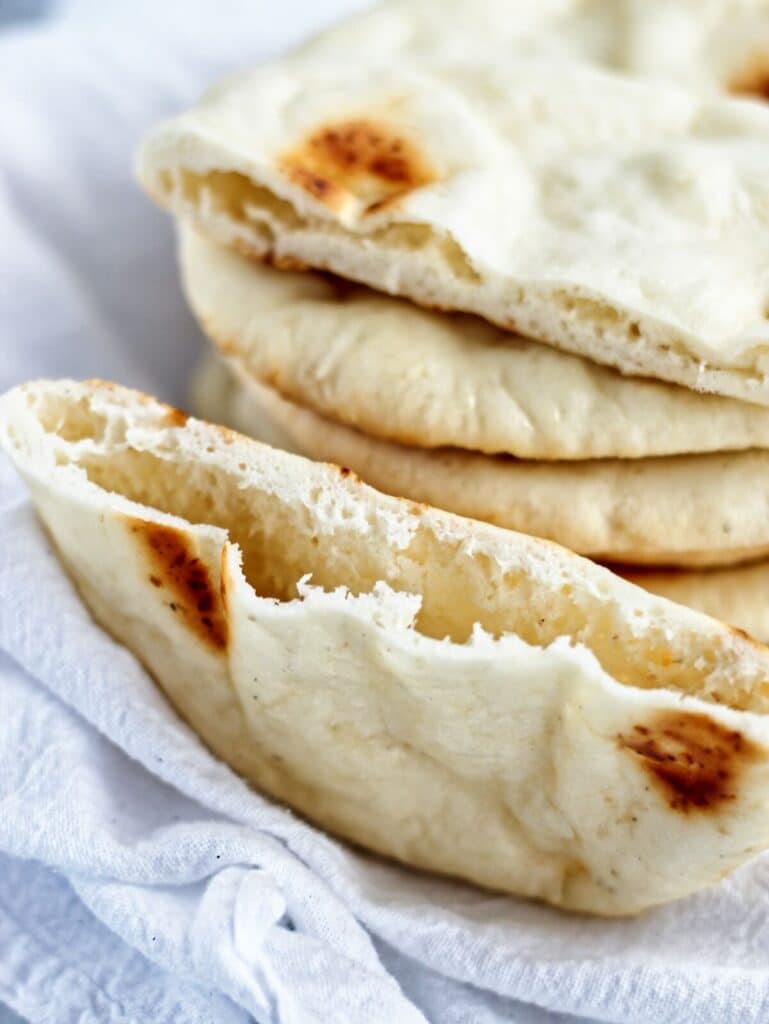 stack of gf pita bread on white towel with one cut in half to show pocket.