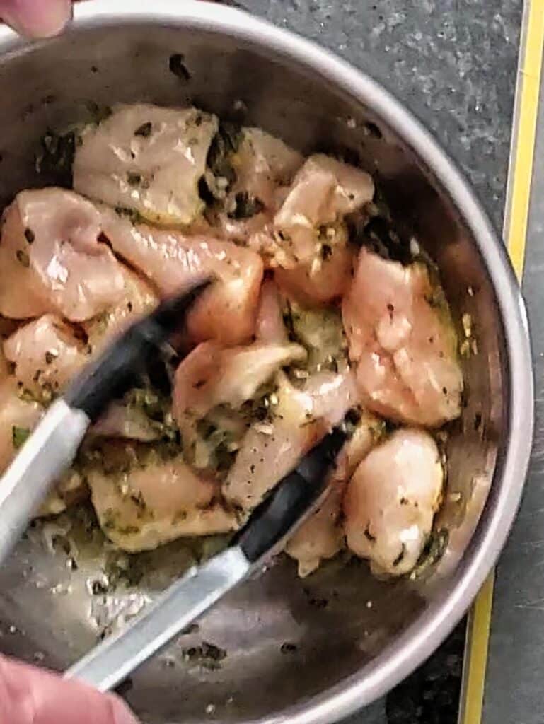 tossing chicken pieces in a stainless steel bowl with marinade.