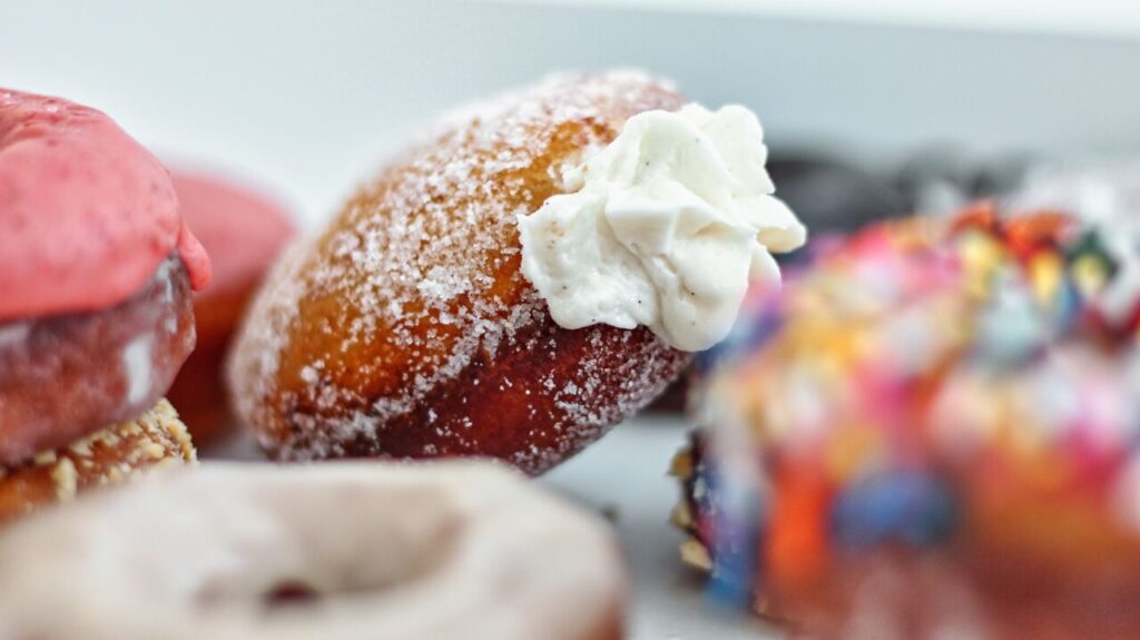 several varieties of gf yeast donuts in white box, focused in on cream-filled donut in the middle.