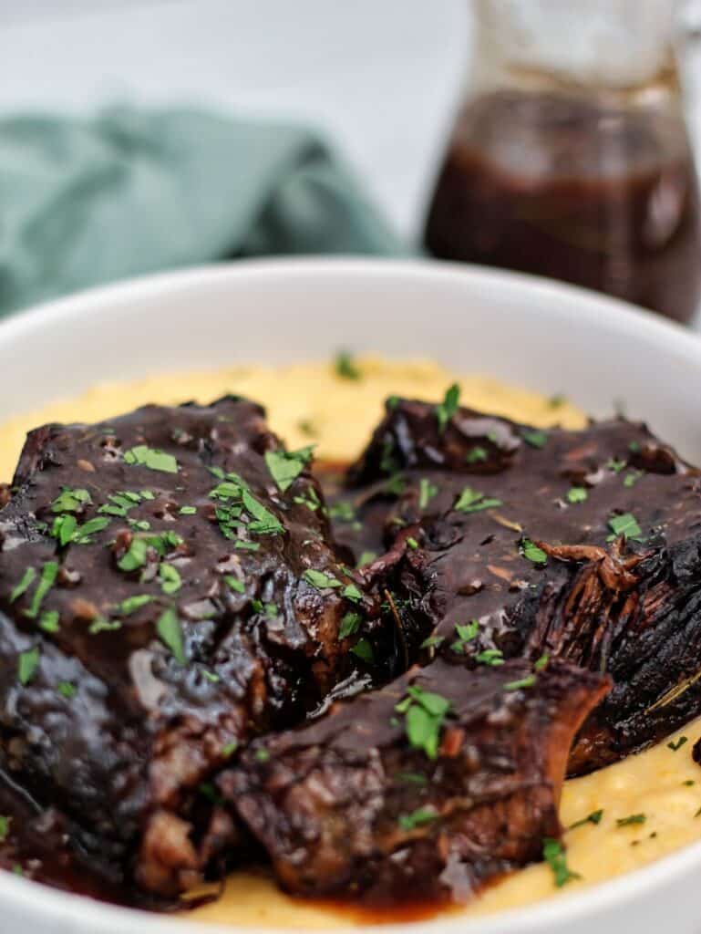 red wine braised pot roast on top of cheesy grits in a white shallow bowl.