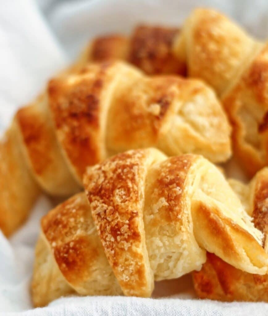 fresh baked gf crescent rolls in white towel-lined basket.