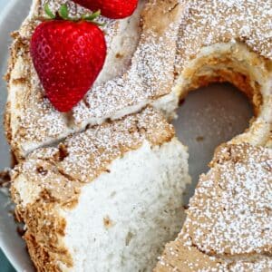 whole gf angel food cake with strawberries and powdered sugar on top with one slice cut out.