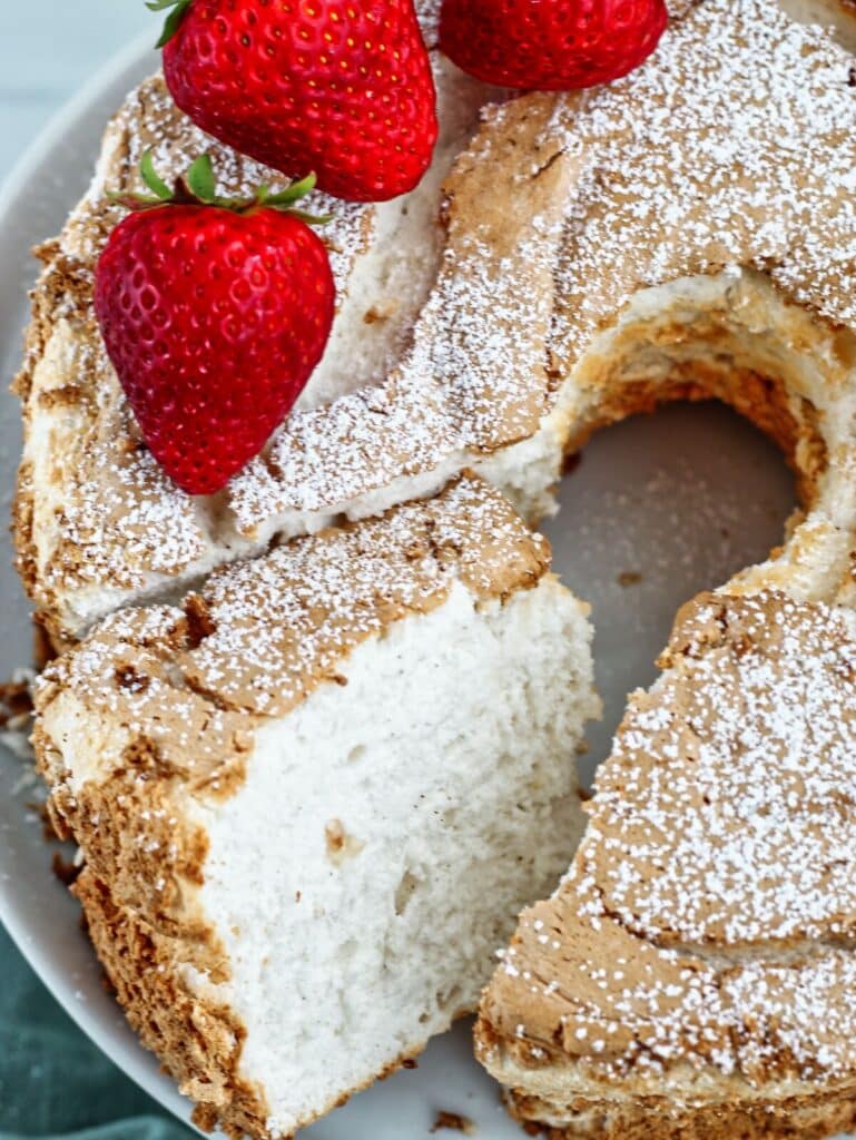 whole gf angel food cake with strawberries and powdered sugar on top with one slice cut out.