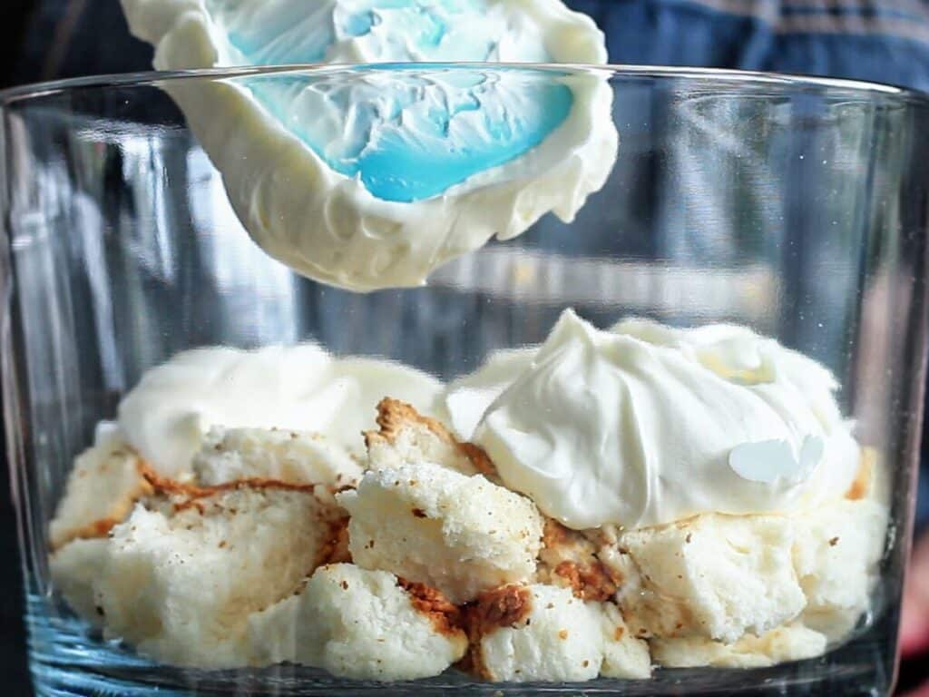 adding cream mixture on top of cake layer in trifle dish.