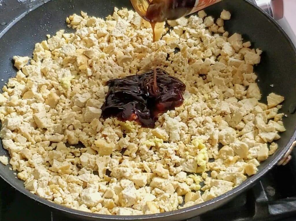 hoisin sauce poured in the middle of a skillet full of tofu crumbles.