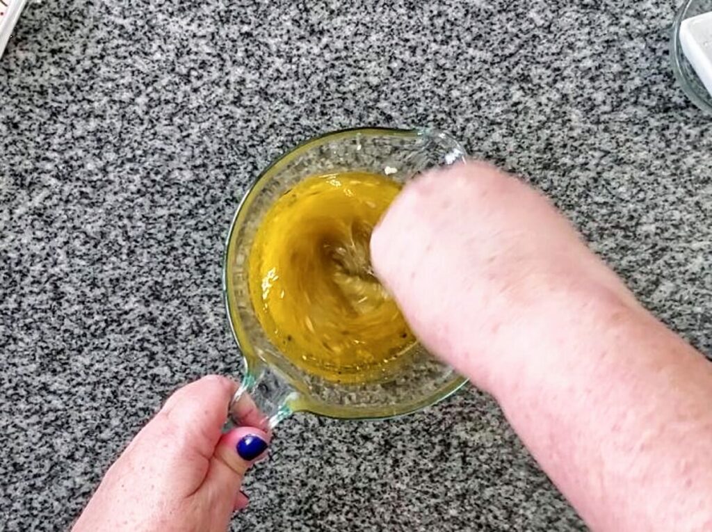 whisking dressing ingredients in small glass measuring cup.