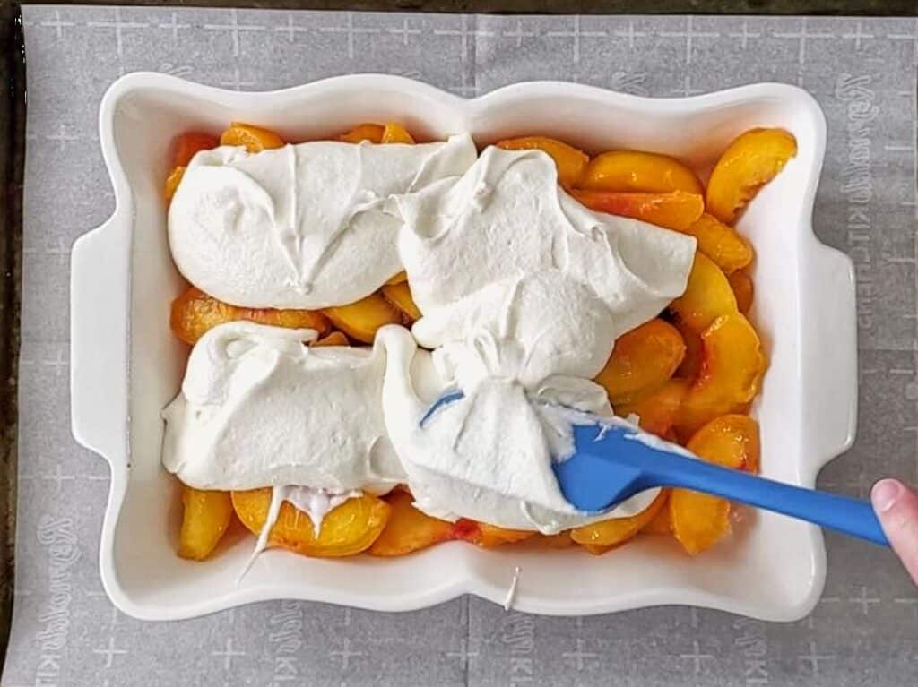 scooping large spoonfuls of batter over peaches.