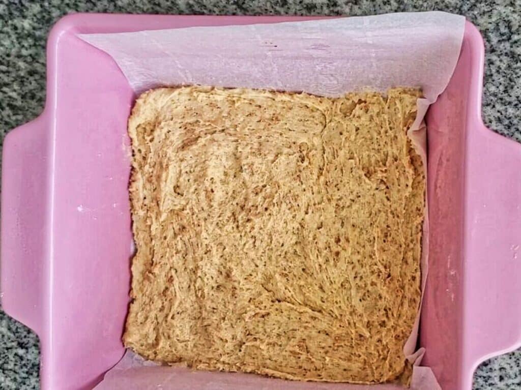 graham cracker cookie dough pressed into parchment-lined pink square baking pan.