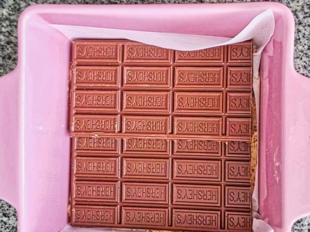 milk chocolate bars on top of crust in pink square pan.