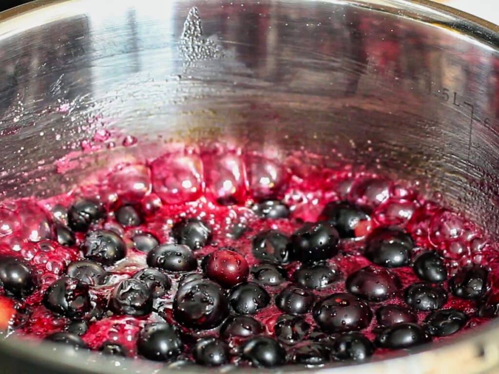 blueberry compote releasing juices and boiling in small saucepan.