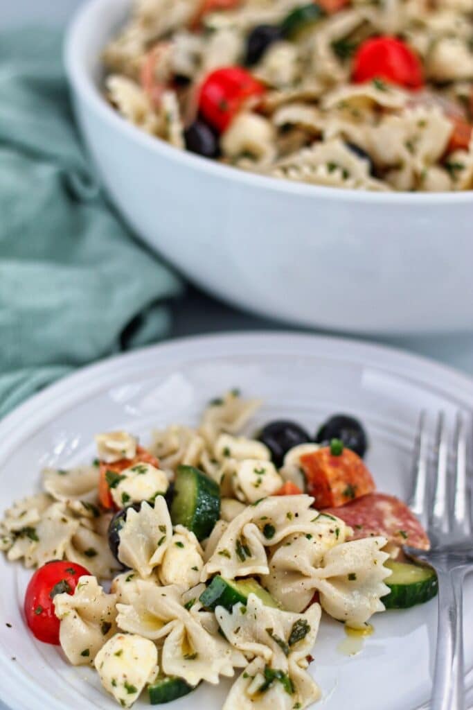 pasta salad on white plate with large white bowl filled with salad in background and sage green towel on the side.
