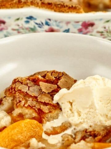 landscape view of shallow white bowl filled with gf peach cobbler and scoop of vanilla ice cream.