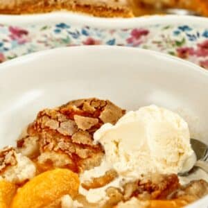 white shallow bowl filled with gf peach cobbler with a scoop of vanilla ice cream.