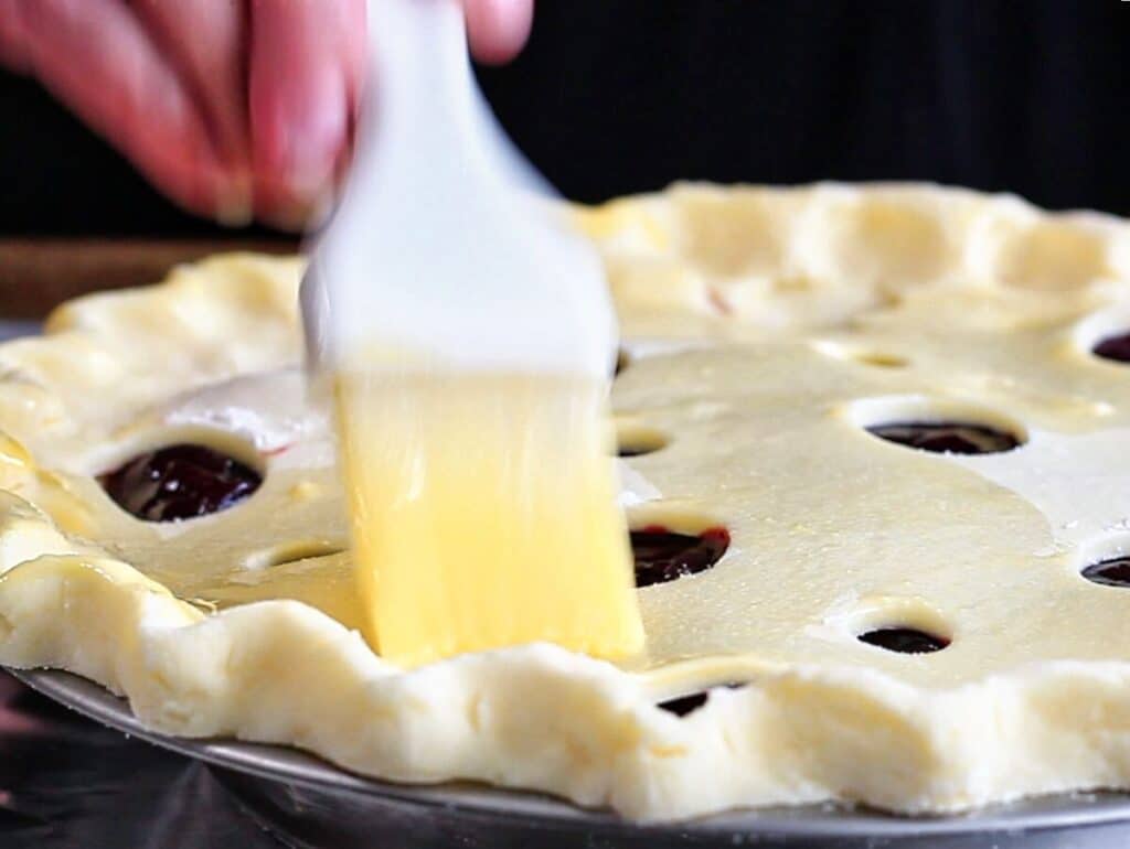 brushing top pie crust with egg wash.