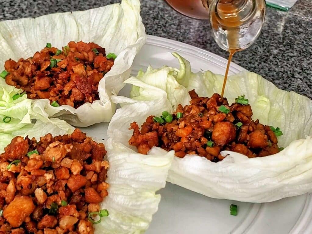 pouring sauce on tofu lettuce wrap on white plate.
