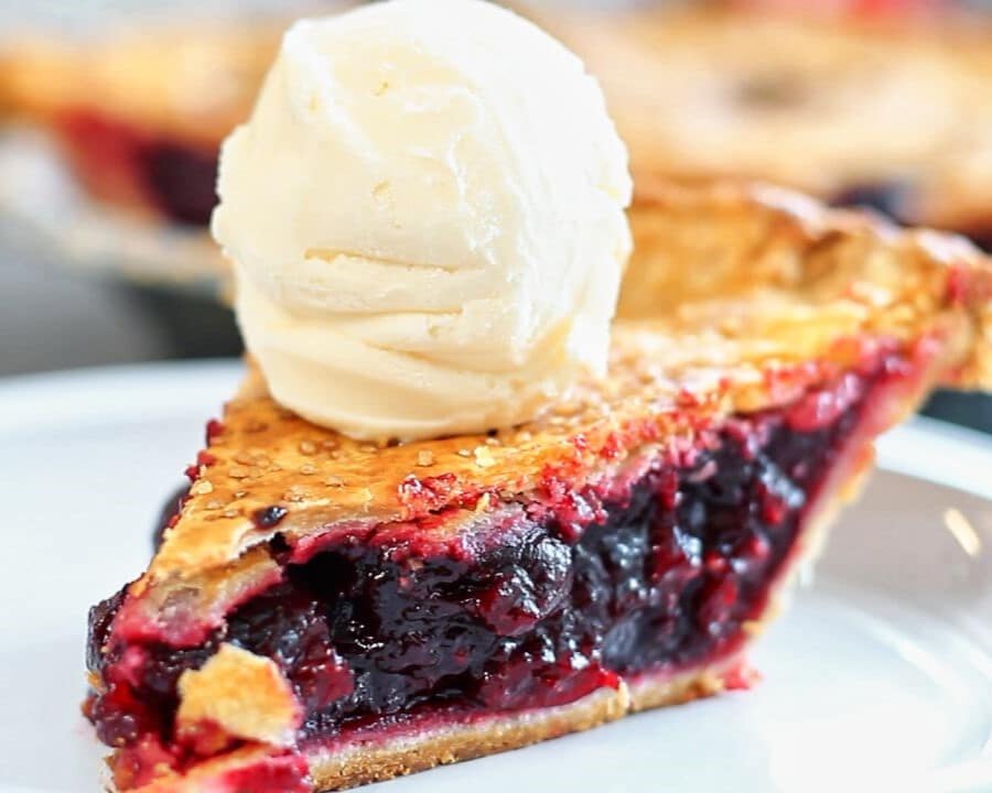 slice of cherry pie on white plate with scoop of vanilla ice cream on top.