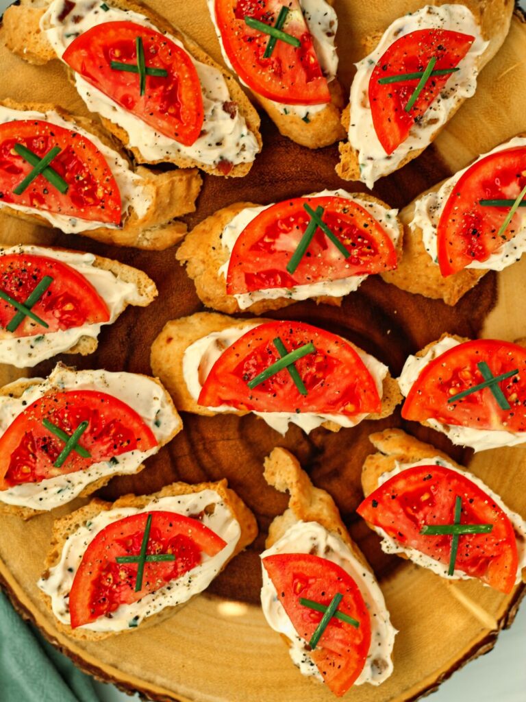several tomato crostini with bacon in a circle on live wood serving platter.
