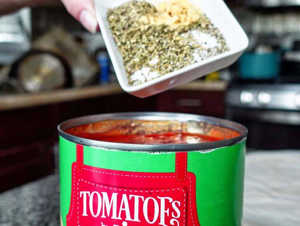 adding herbs to crushed tomatoes in large can.