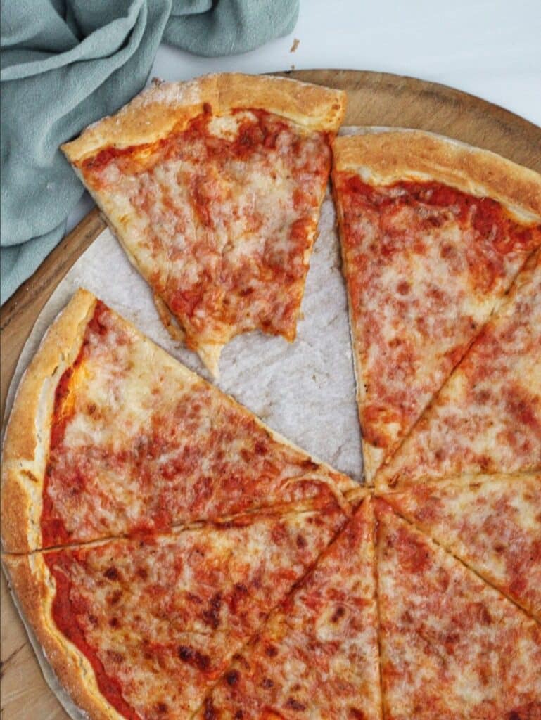 overhead pic of whole pizza cut up on wooden pizza peel with green towel in the background and one bite taken out of one slice.