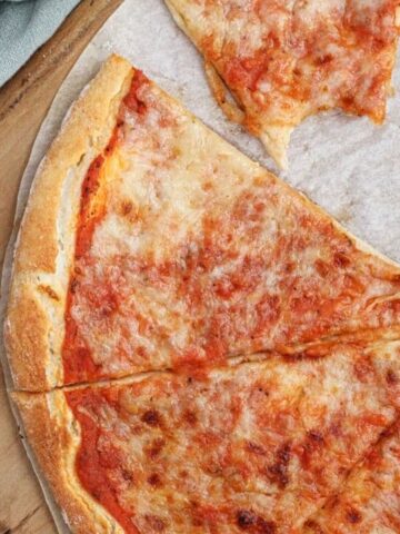 landscape overhead view of whole pizza cut into triangles on wooden pizza peel with green towel to the side and a bite taken out of one slice.