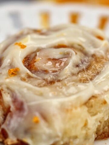 landscape view of one orange cinnamon roll on a white plate with scalloped edges.