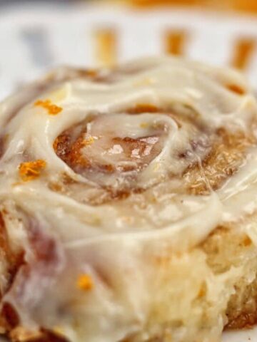 landscape view of one orange cinnamon roll on a white plate with scalloped edges.