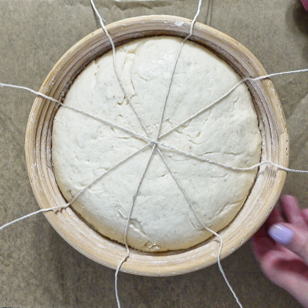 4 strings placed over top of risen dough in banneton.
