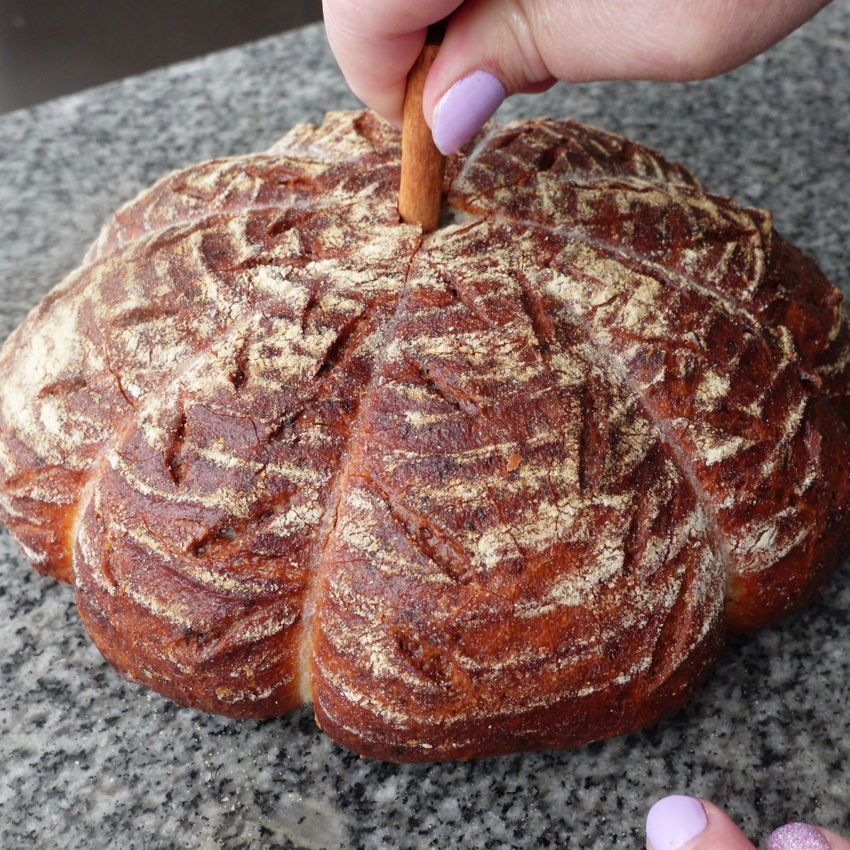 pushing cinnamon stick into the middle of baked and cooled pumpkin shaped bread.