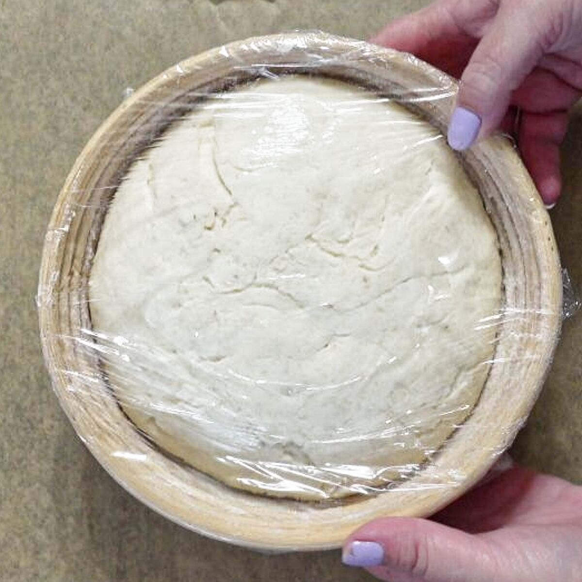 risen dough in banneton covered in plastic.