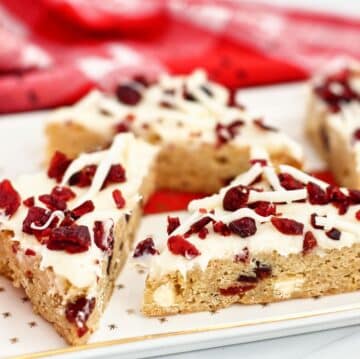cranberry bliss bars on white platter with red checked napkin in the background.