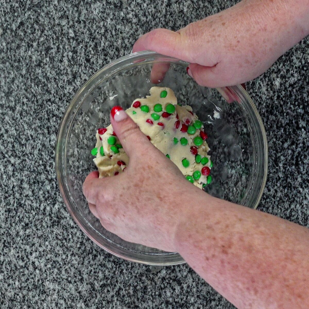folding mini red and green M&Ms into cookie dough in glass bowl.