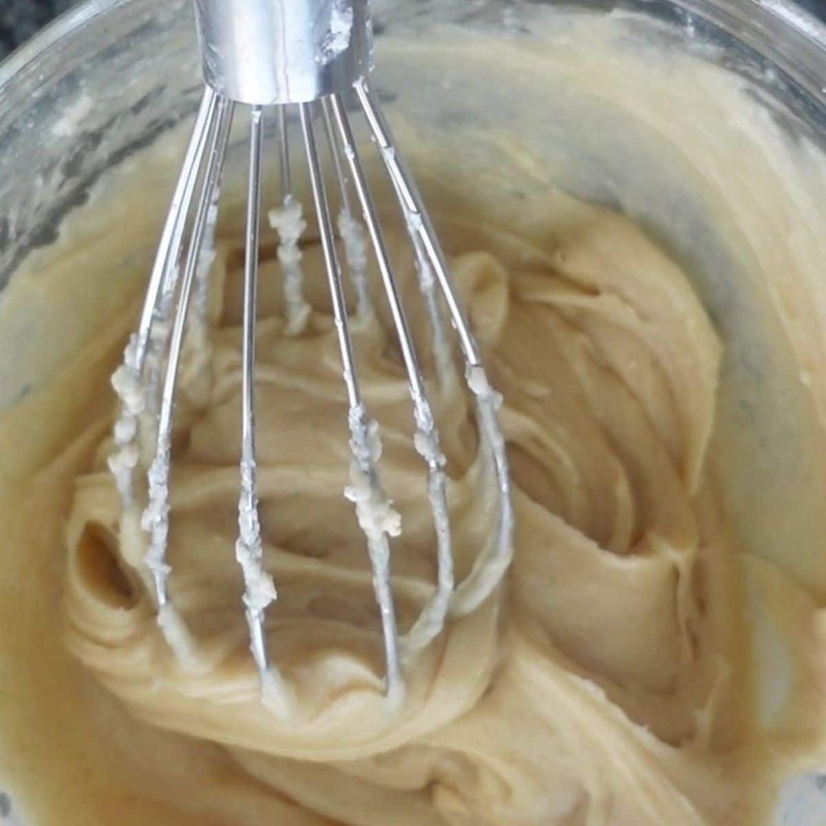 mixing brown butter cream cheese frosting in glass bowl with whisk.
