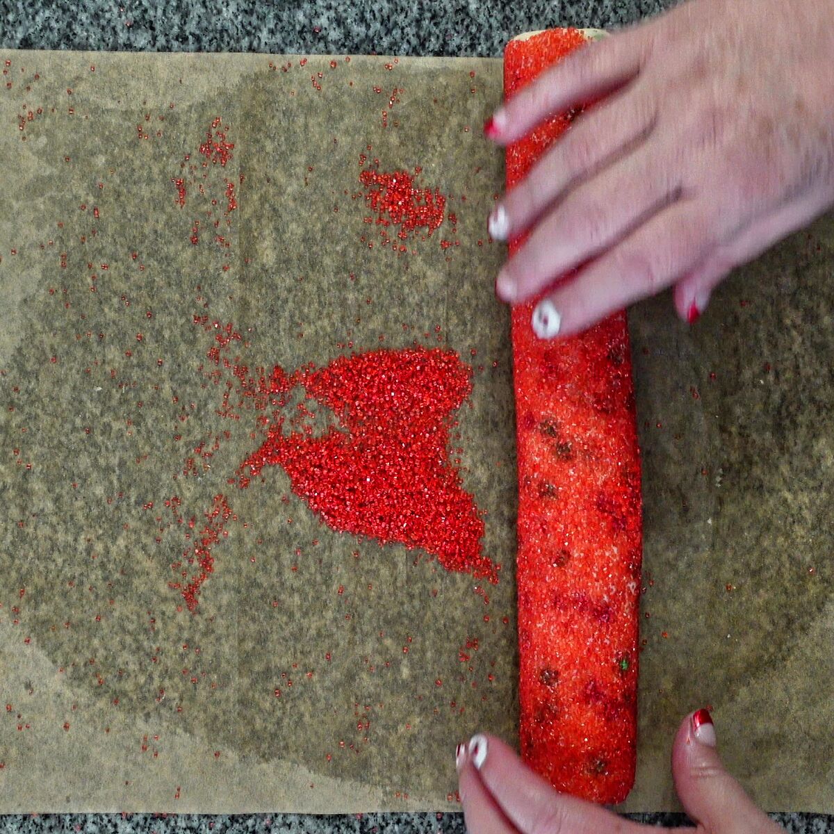 rolling log of dough into red colored sugar on parchment.