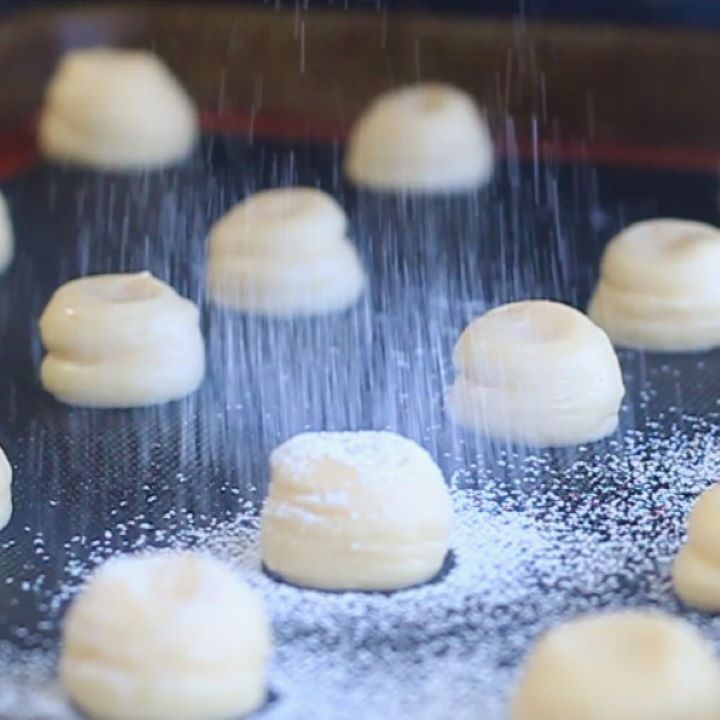 sifting powdered sugar over flattened cream puffs.